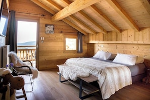 Ein Schlafzimmer einer Holzhütte mit einem Bett, einem Sessel und Blick durch eine Tür.