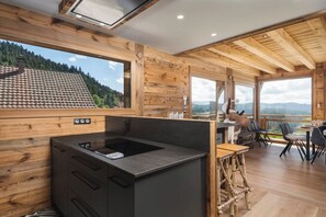 Eine moderne Küche mit Einbauherd, Holzwänden und einem großen Fenster mit Blick auf eine gebirgige Landschaft.