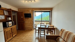 Una cucina funzionale con mobili in legno, un tavolo da pranzo con sedie e un divano. Un'ampia finestra si affaccia su un paesaggio montuoso.