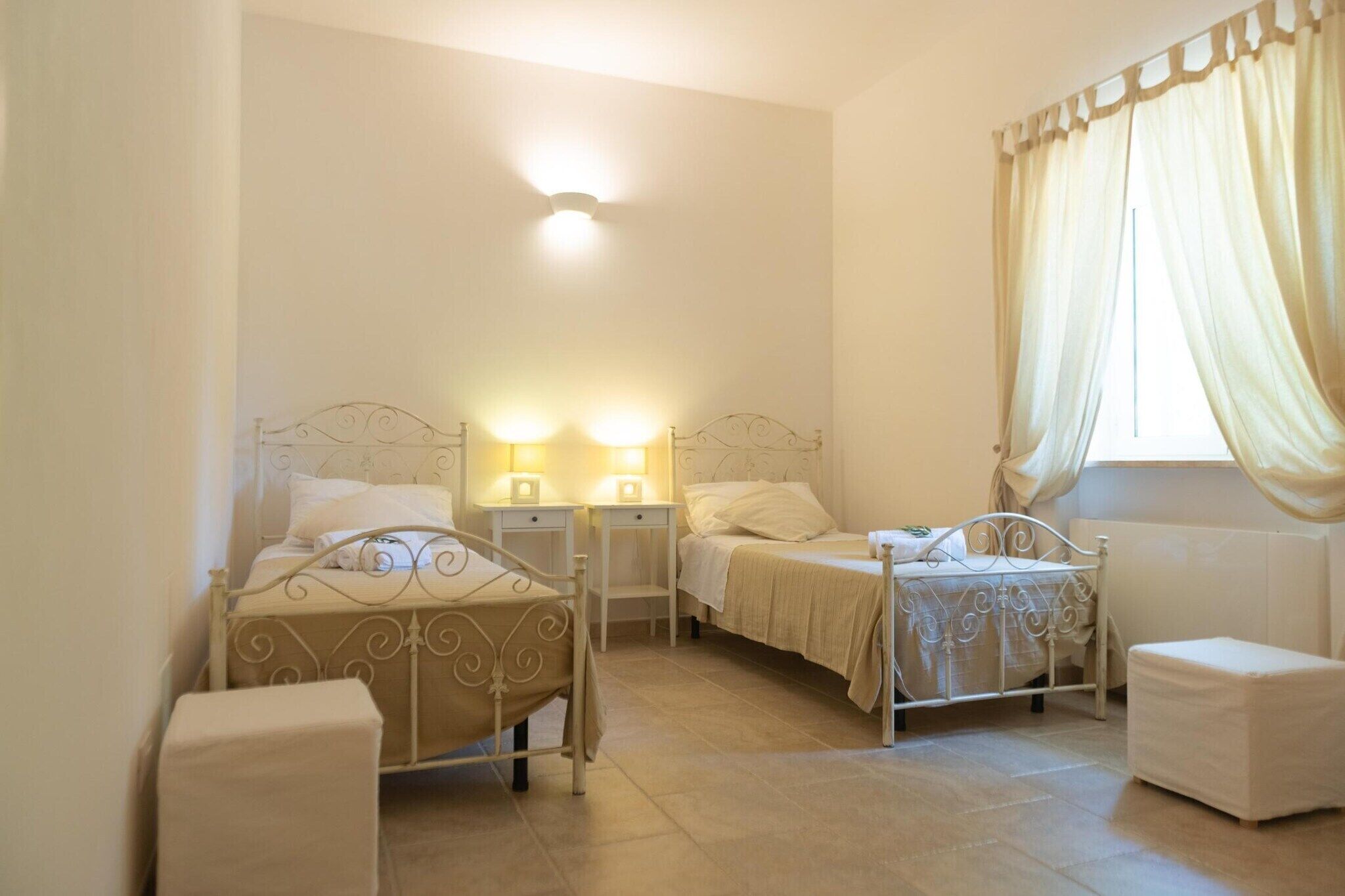 A bedroom with two beds, bedside tables, and a window with curtains.