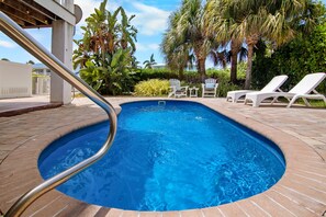 Une piscine avec un escalier en métal, entourée de chaises longues et de palmiers.