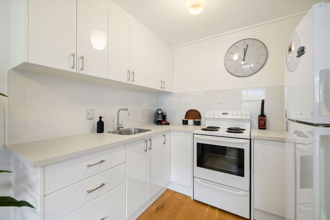 A modern kitchen with white cabinets, a stainless steel sink, a stove, and a clock on the wall.