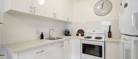 A modern kitchen with white cabinets, a stainless steel sink, a stove, and a clock on the wall.
