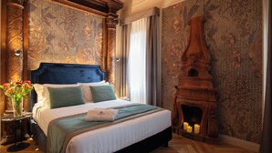 Une chambre à coucher avec un grand lit, une tête de lit en bois sculptée, une cheminée et un papier peint à motifs.
