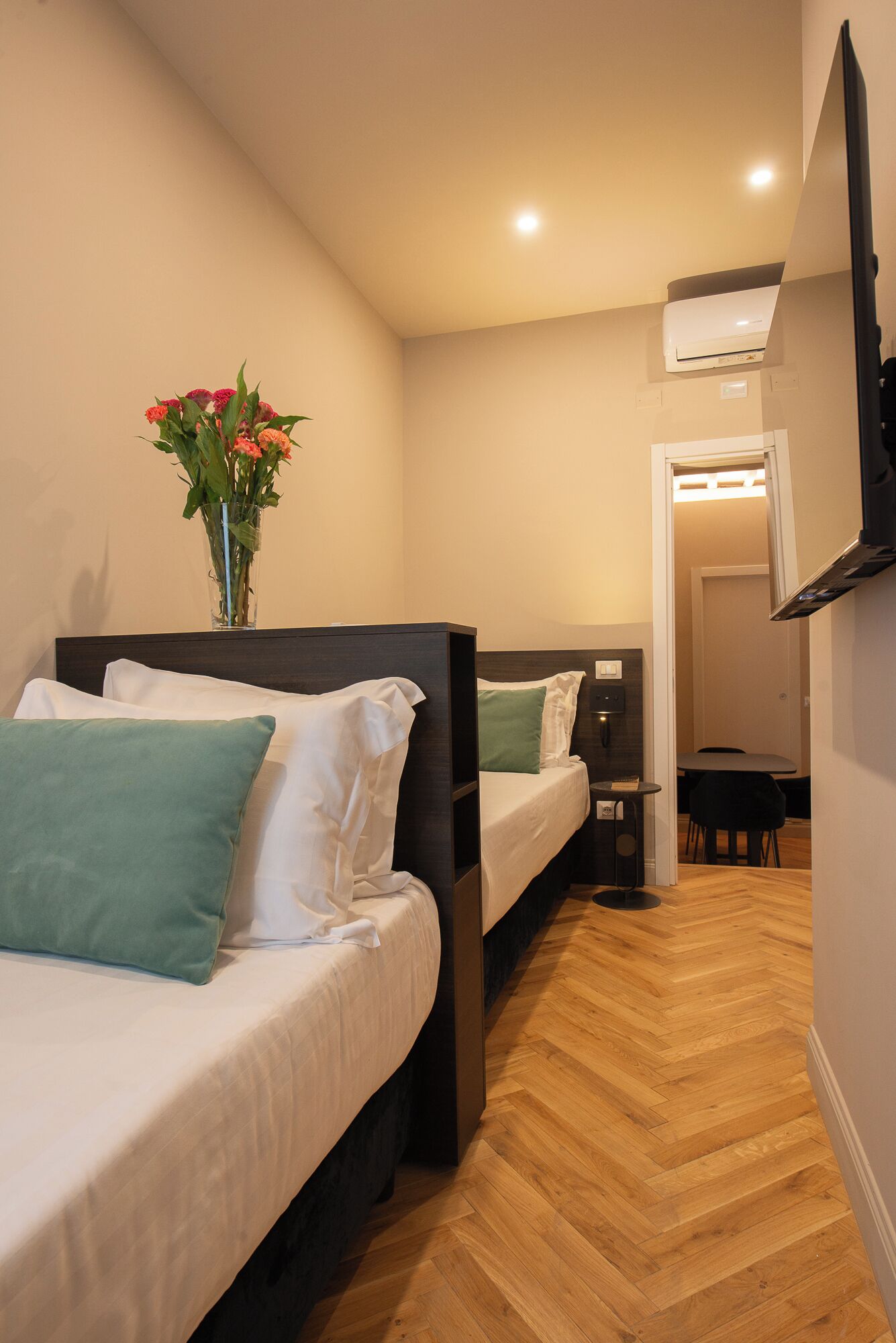 Een hotelkamer met twee bedden, een tafeltje, een stoel en een televisie aan de muur.