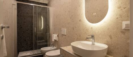 A modern bathroom with a glass-enclosed shower, a toilet, and a large oval sink with a mirror above.