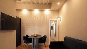 Un salon moderne avec un canapé noir, une table à manger avec des chaises et un téléviseur fixé au mur.