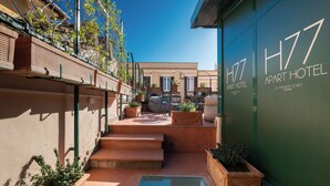 Une cour avec une piscine, des espaces de détente en plein air et un bâtiment portant l’inscription « H77 Apart Hotel ».