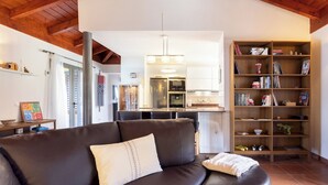 A modern living room with a brown leather sofa, a wooden bookshelf, and a kitchen in the background. - Home2Book Coastal Dream Villa in Tacoronte (Tacoronte)