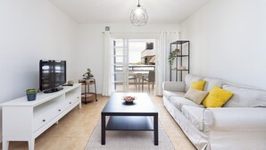 Un soggiorno moderno con TV, tavolino, divano con cuscini gialli, lampada a sospensione geometrica e vista all'esterno.