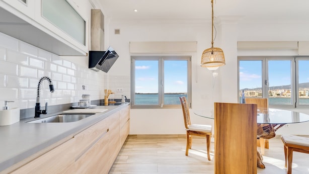 A modern kitchen with a large window, wooden cabinets, and a dining area with a glass table and chairs.