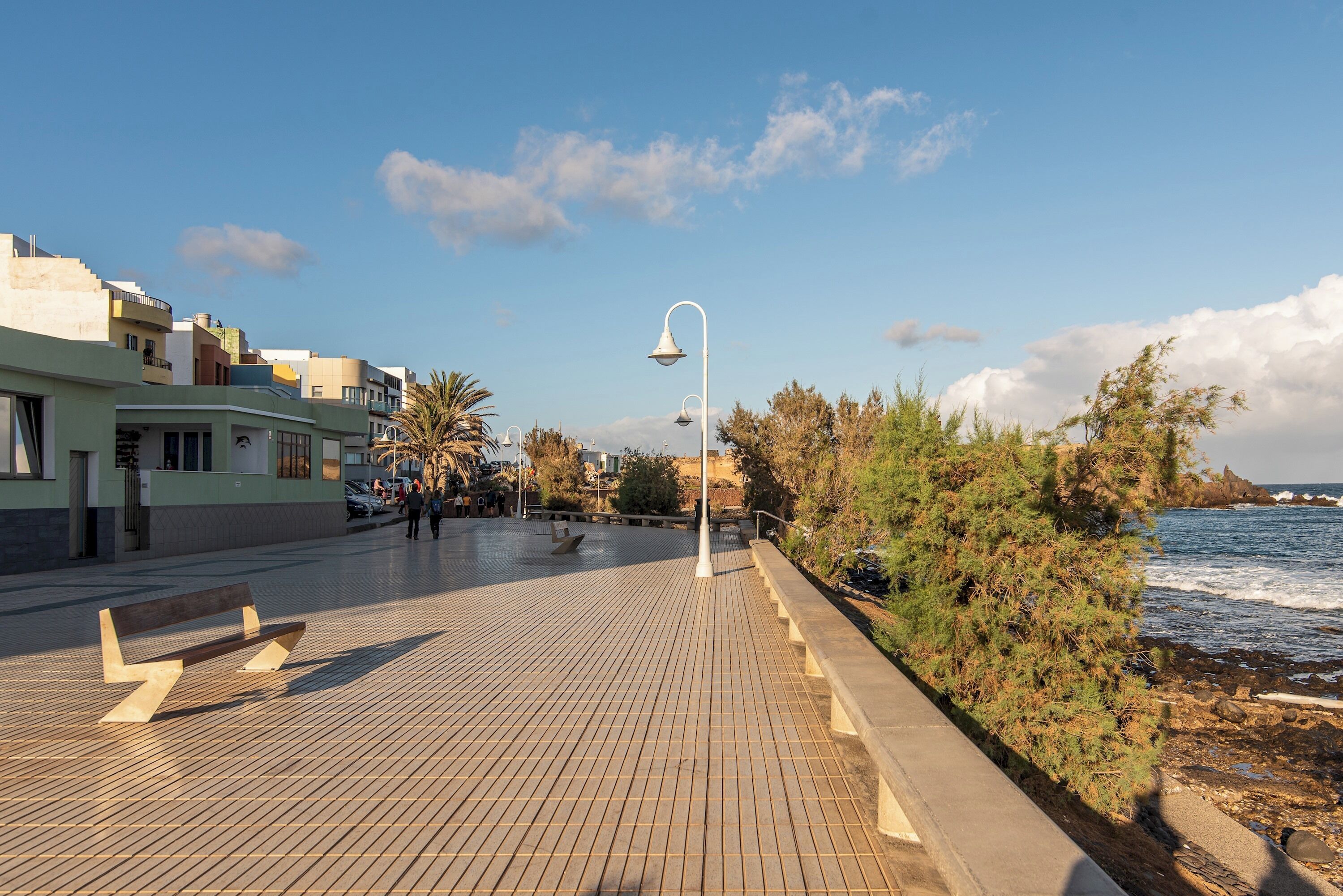 Une promenade dallée avec des bancs, un lampadaire et des bâtiments le long d’une zone côtière.