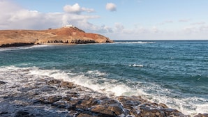 A coastal landscape with rocky terrain, a lighthouse on a hill, and the sea.