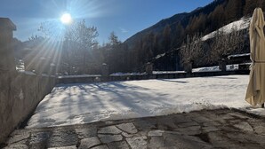 Un patio nevado con suelo de piedra, un muro de piedra y una montaña al fondo.