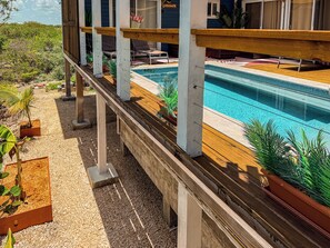 A pool with a wooden deck, surrounded by potted plants and a clear view of the sky.