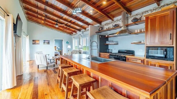 Een ruime keuken met een houten kookeiland, barkrukken en een hoog plafond met zichtbare balken.