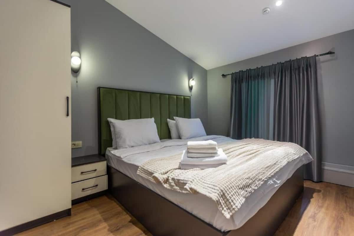 Une chambre à coucher moderne avec un grand lit, une tête de lit verte et une table de chevet avec une lampe.
