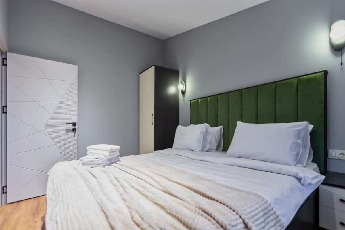Une chambre d’hôtel moderne avec un lit soigneusement fait, une tête de lit verte et un luminaire fixé au mur.