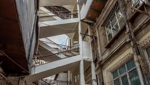 Un bâtiment à plusieurs niveaux avec un escalier central, une enseigne indiquant « ZOO MAQAZIN », et une personne qui pousse un chariot.