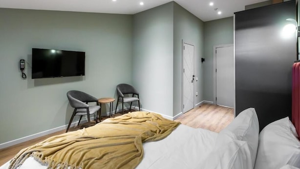 Une chambre d’hôtel moderne équipée d’un lit, d’une télévision, de deux fauteuils, d’une petite table et d’une armoire.