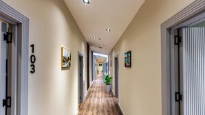 Un couloir d’hôtel avec un plancher en bois, des portes numérotées et des œuvres d’art encadrées accrochées aux murs.