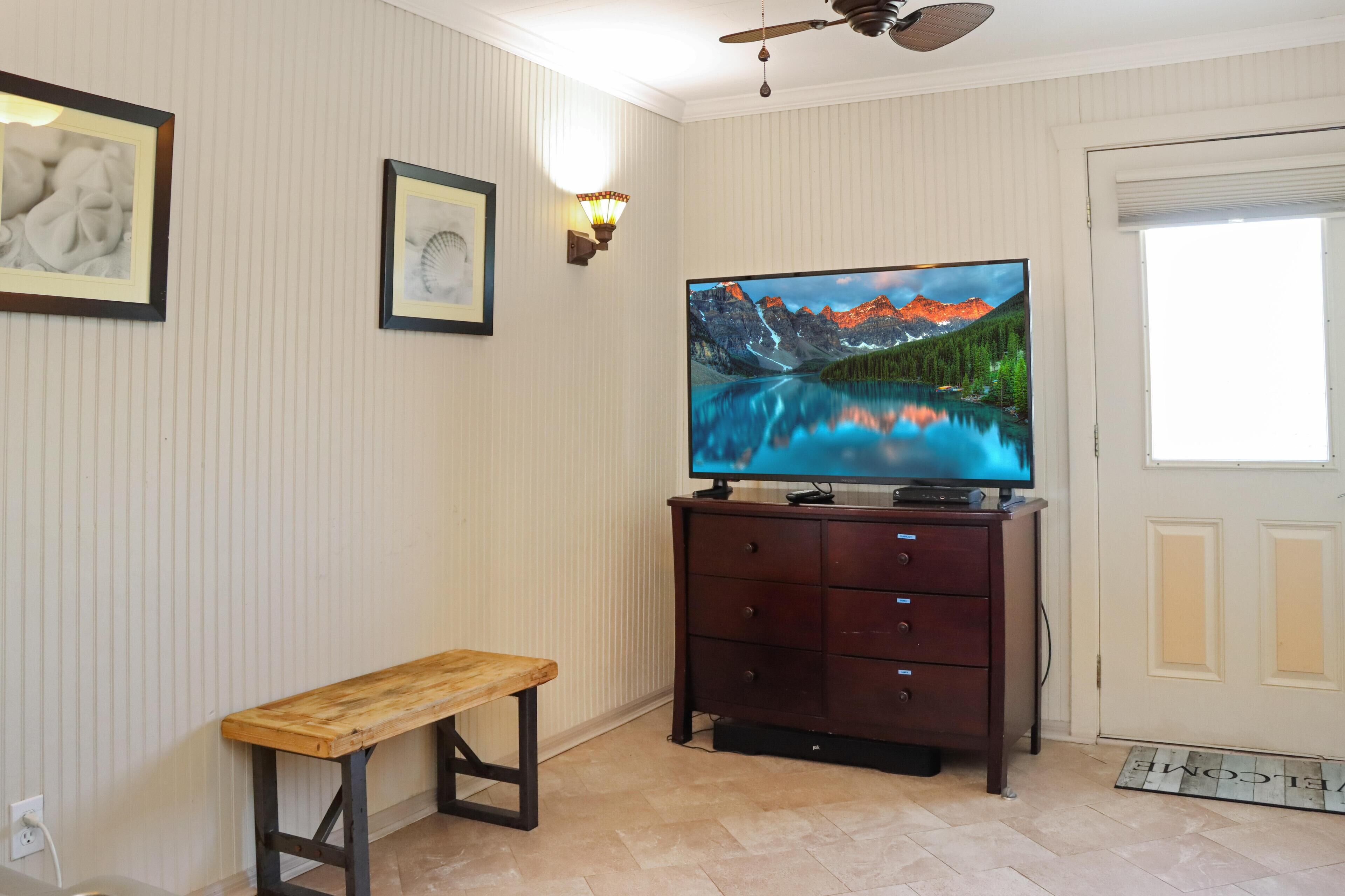 A room with a television on a wooden cabinet, a bench, and a door with a doormat.