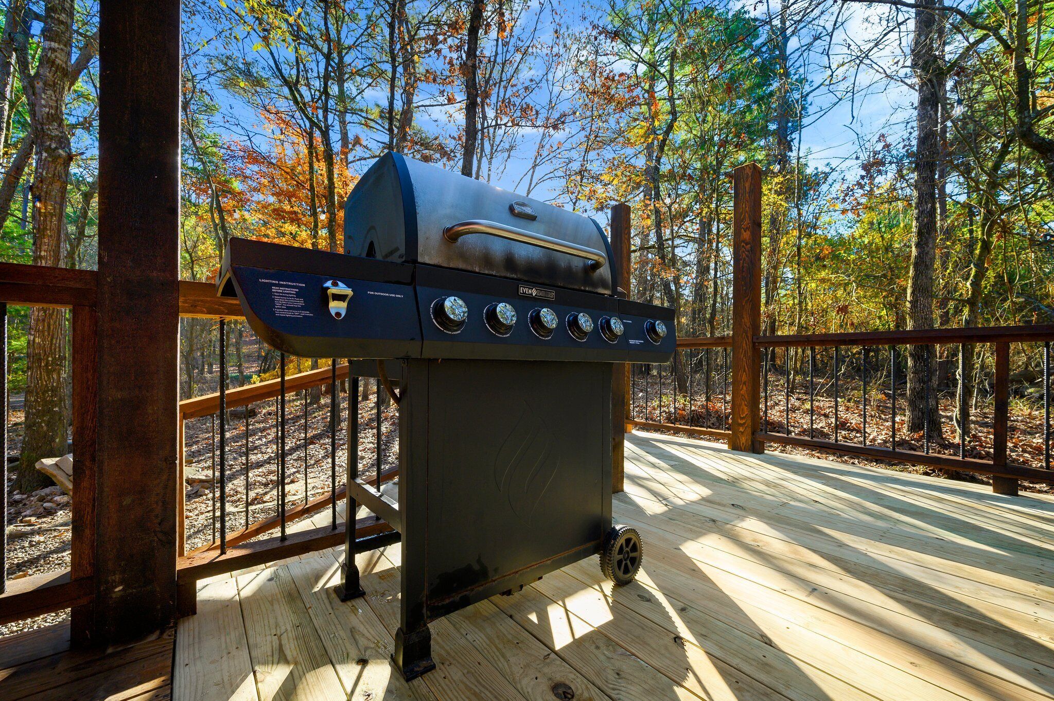 A portable grill on a wooden deck with a view of trees and a clear sky.