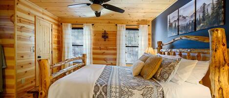 A wooden cabin bedroom with a bed, a ceiling fan, and a wall with three framed pictures.