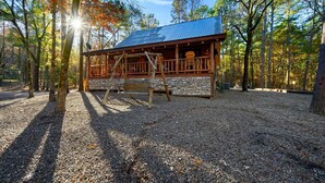 A cabin with a stone foundation, wooden deck, and a metal roof, surrounded by a forest.