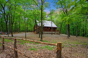 Una cabaña rodeada de bosque, con un camino de grava que conduce a ella.