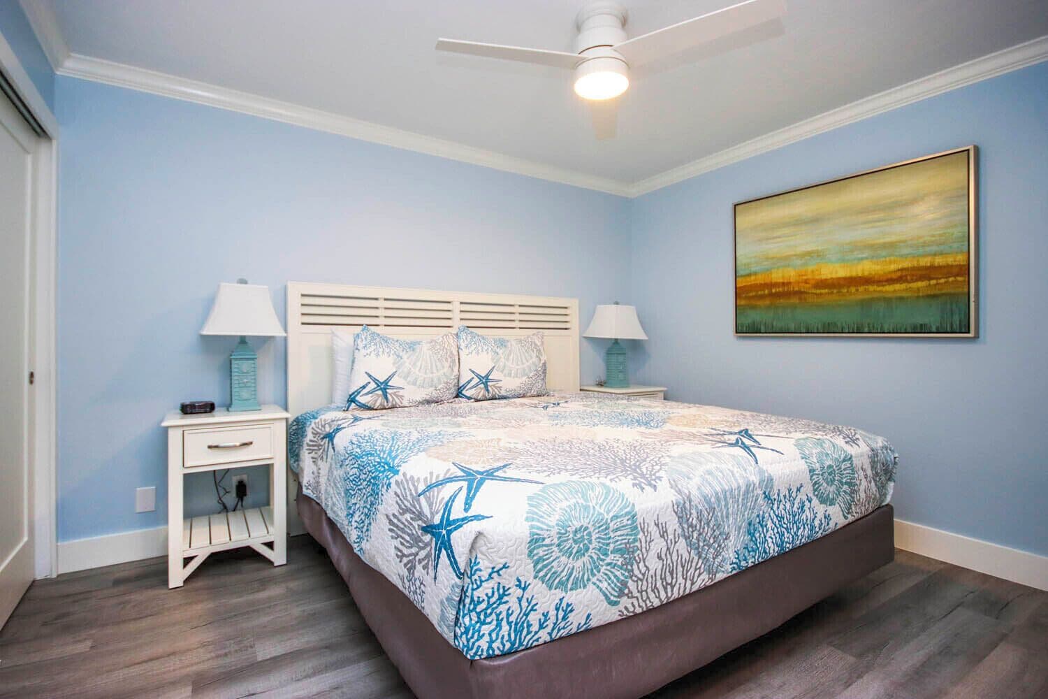 A bedroom with a bed, nightstands, a ceiling fan, and a painting on the wall.