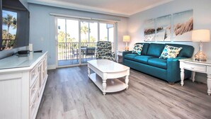 A spacious living room with a blue sofa, a white coffee table, and a TV on a white cabinet.