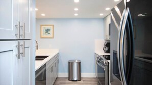 A modern kitchen with stainless steel appliances, a trash can, and a framed picture on the wall.
