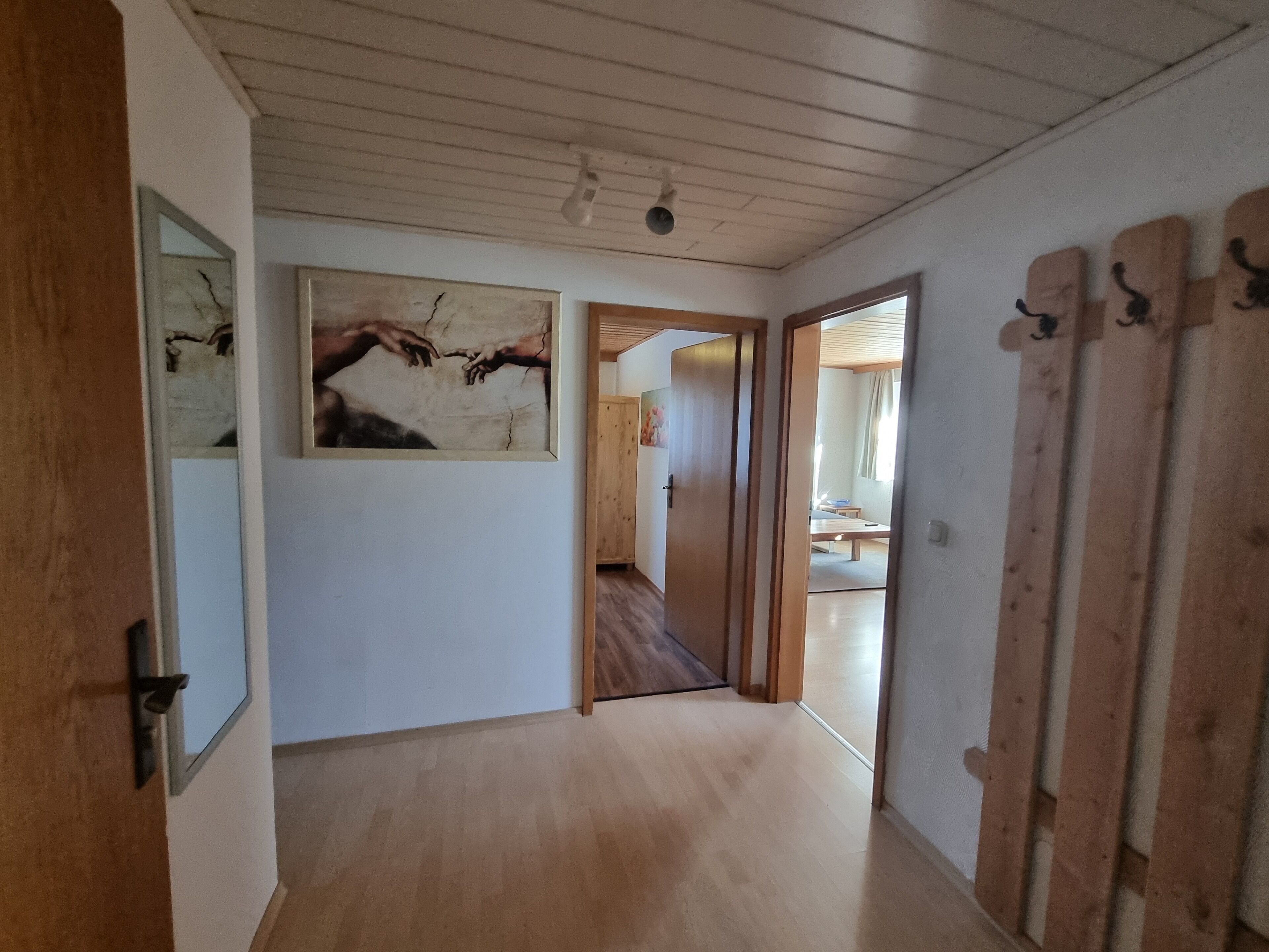 A hallway with wooden flooring, a painting on the wall, and a door leading to another room.