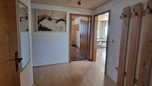 Un couloir doté d’un plancher en bois, un tableau accroché au mur et une porte donnant sur une autre pièce.