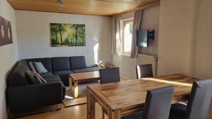 Un salon moderne avec un canapé, une table à manger en bois et un téléviseur fixé au mur.