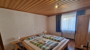 Une chambre à coucher avec un lit en bois, une table de chevet, une lampe, une fenêtre avec des rideaux et une armoire.