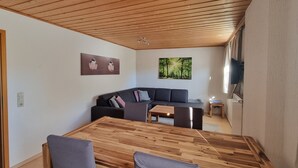 Un salon moderne avec un plafond en bois, un canapé gris foncé, une table à manger en bois et deux tableaux accrochés aux murs.