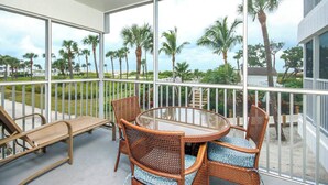 Ein Balkon mit Korbmöbeln, einem Glastisch und Blick auf Palmen sowie einen Strand.