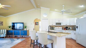 A spacious kitchen with white cabinets, a central island with bar stools, a microwave, and a refrigerator.