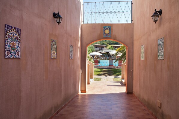 Un pasillo con paredes de baldosas y vista a un área de estar exterior y una piscina.