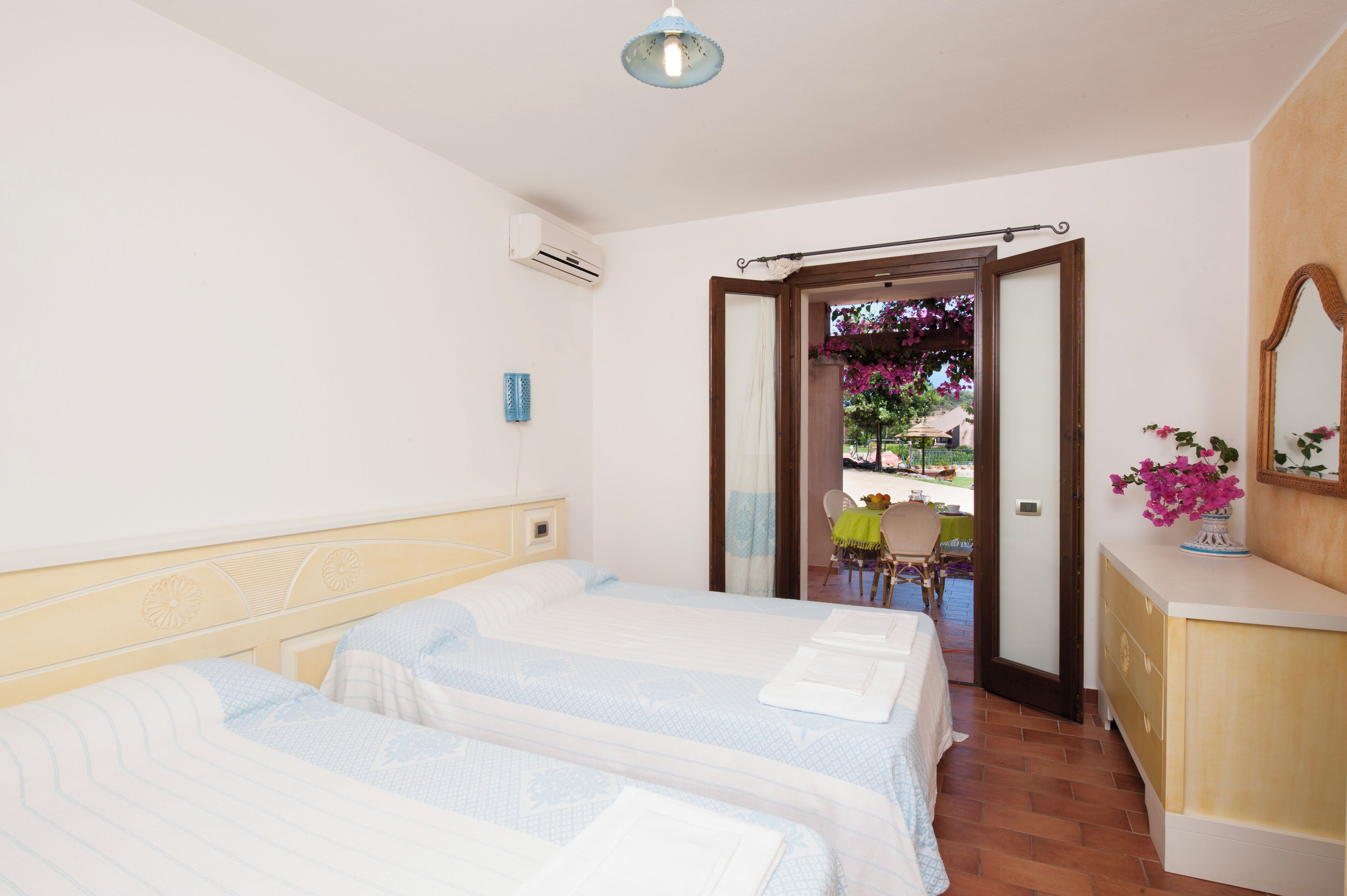 Een hotelkamer met twee bedden, een houten hoofdeinde, een kleine tafel met een stoel, een spiegel en uitzicht op het balkon.