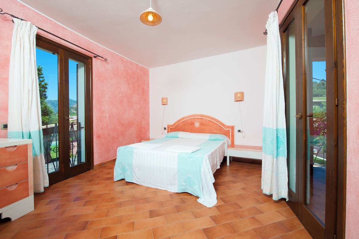 Une chambre à coucher avec un lit, une commode, une table de chevet et une fenêtre avec des rideaux.