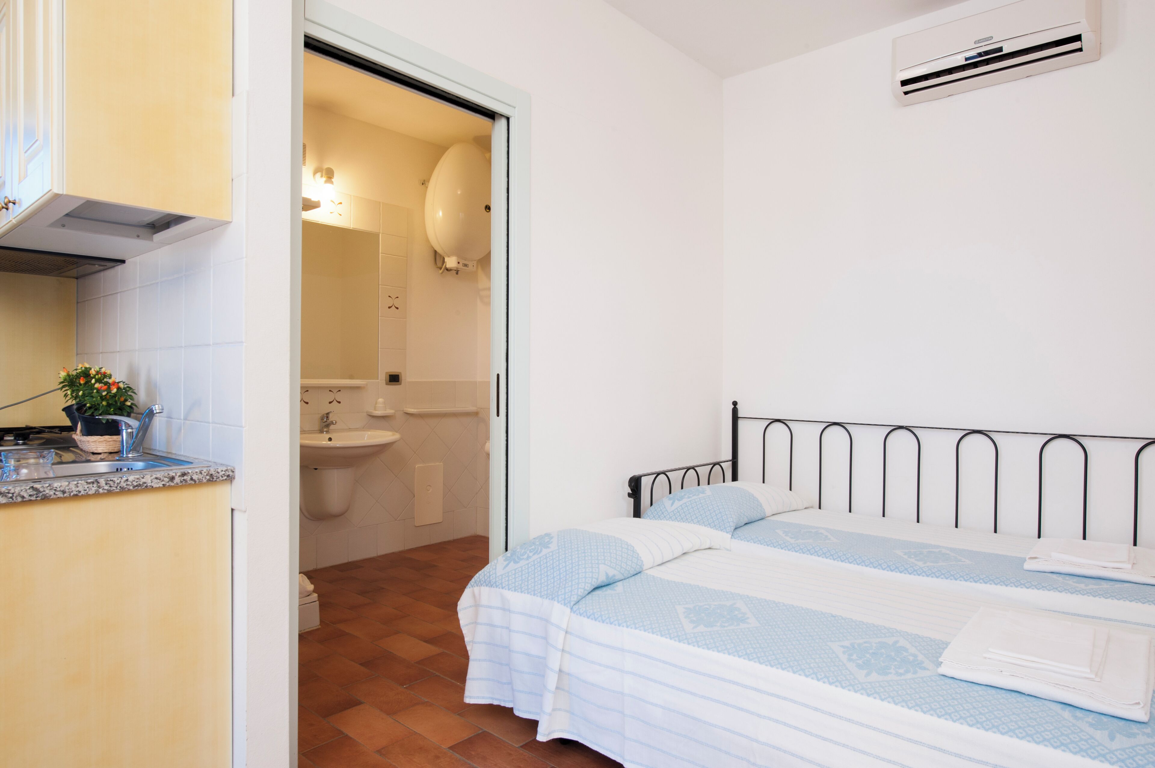 A bedroom with a bed, a bathroom with a sink and toilet, and a kitchen area with a stove and sink.
