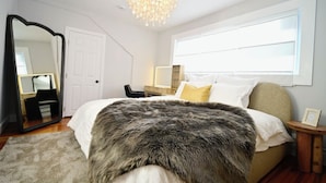 A bedroom with a large bed, a mirror, a chandelier, a window, and a bedside table. - Westshore Luxury (West Haven)