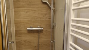 Ducha con pared de paneles de madera, cabezal de ducha de mano y panel de control montado en la pared.
