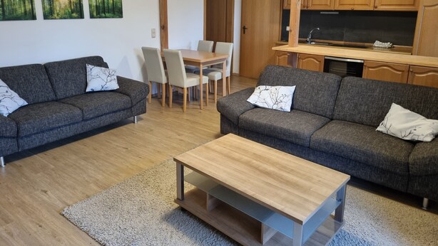 Una sala de estar moderna con dos sofás grises, una mesa de centro de madera y un comedor con mesa y sillas.