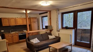 Un espacio habitable compacto con kitchenette, sofá, mesa de centro y un ventanal que proporciona luz natural.