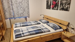 Una cama de madera con dos almohadas y una colcha, una mesita de noche con una lámpara, un radiador y una ventana con cortina.