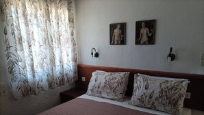 A bedroom with a bed, floral curtains, two wall-mounted lights, and two framed pictures.